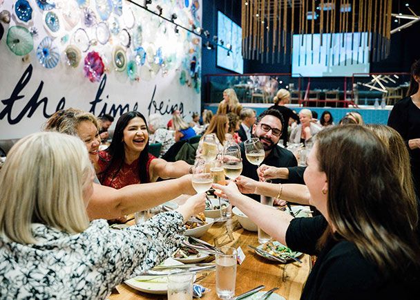 A group of people raising their wine glasses in a toast at a dinner table during a Retreats Resources roadshow.