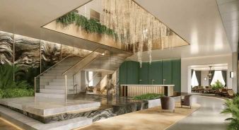 Modern hotel lobby at Fairmont New Orleans, with marble staircase, green accent wall, lush plants, water feature, and chandelier with cascading lights hanging from the ceiling.
