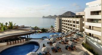 Corazon Cabo Resort & Spa, Cabo San Lucas, with an outdoor pool, sun loungers, and umbrellas overlooks the ocean and distant rocky hills under a partly cloudy sky.