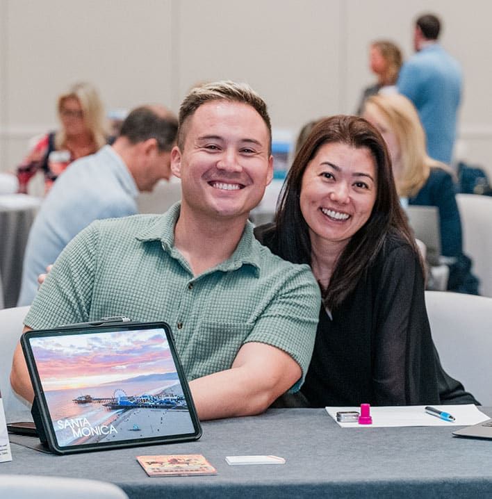 A smiling man and woman sit at a table with an iPad displaying an image of Santa Monica.